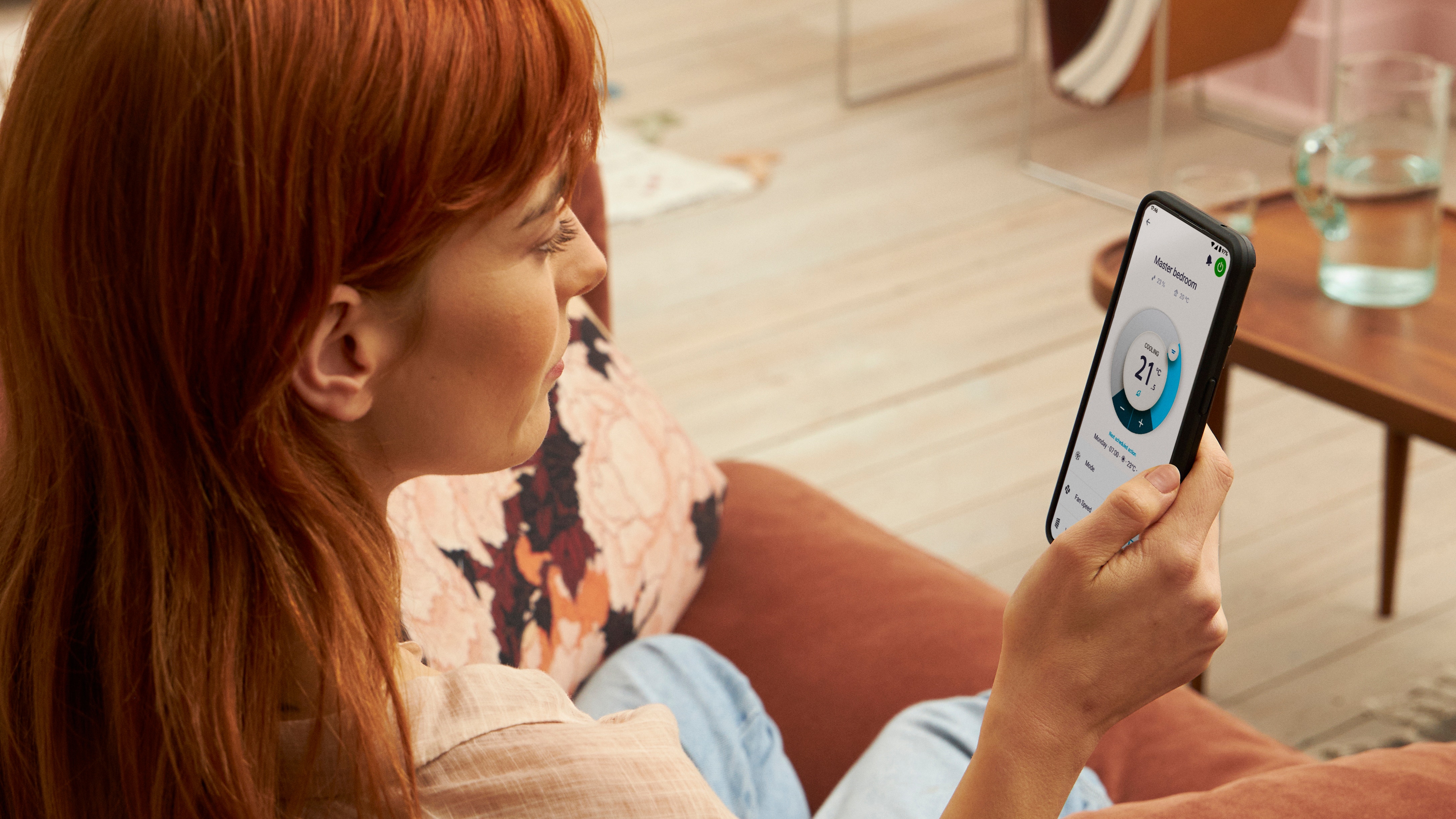 Kvinde, der holder en smartphone og bruger Onecta-appen til at styre rumtemperaturen.