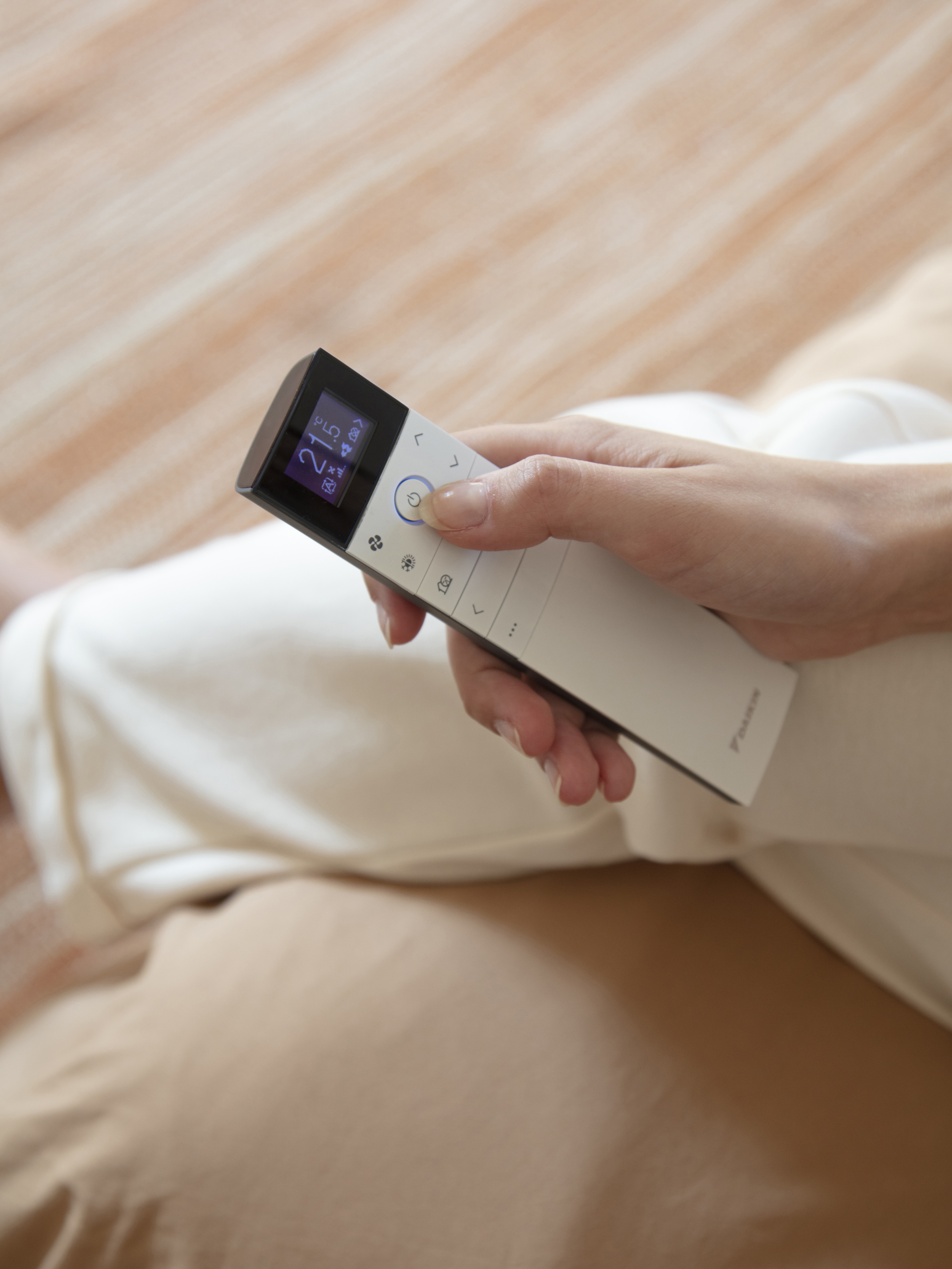 Kvinde, der sidder i sofaen og styrer sit klimaanlæg med fjernbetjeningen