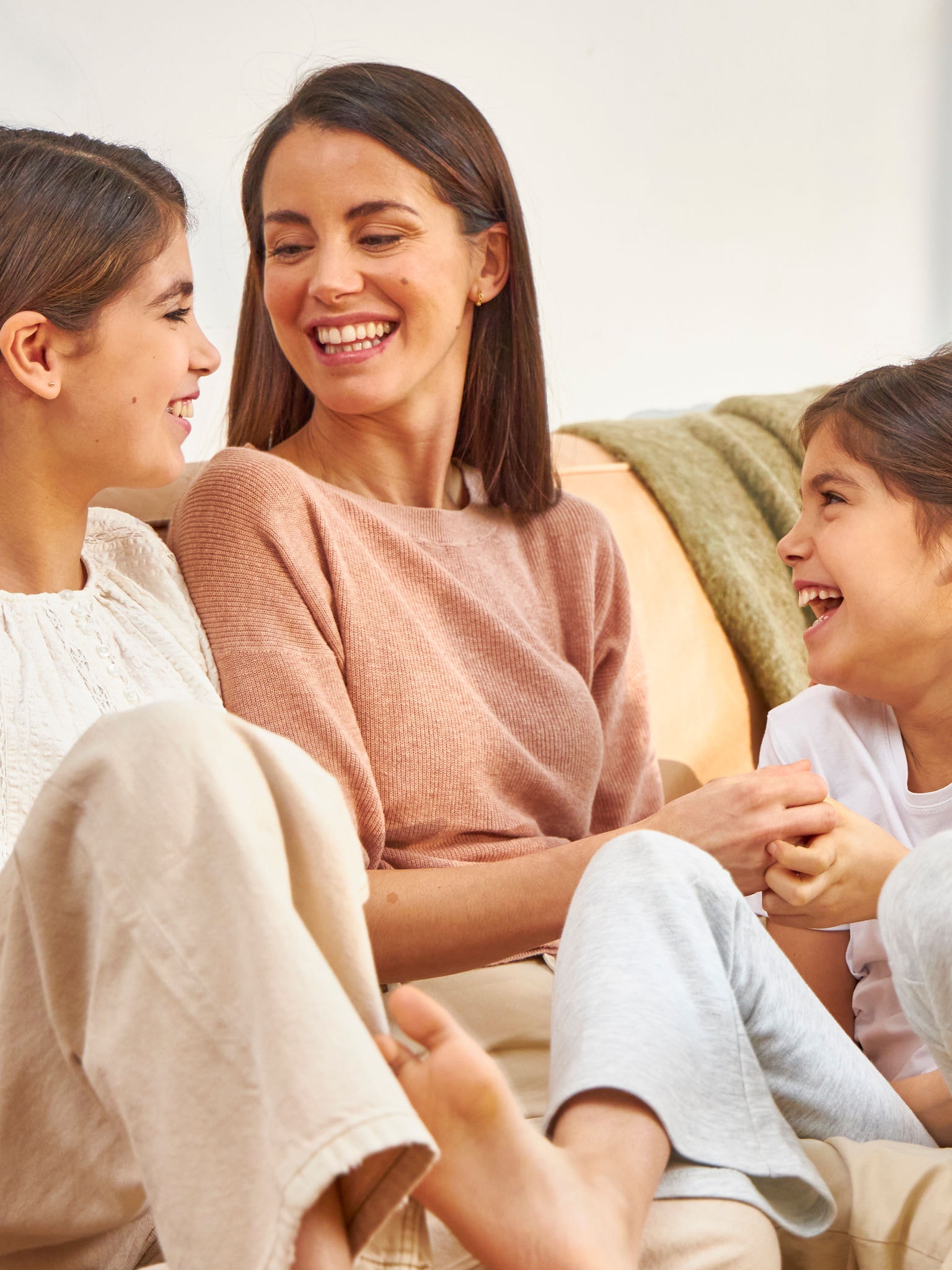 En mor og hendes to døtre sidder i sofaen og griner.