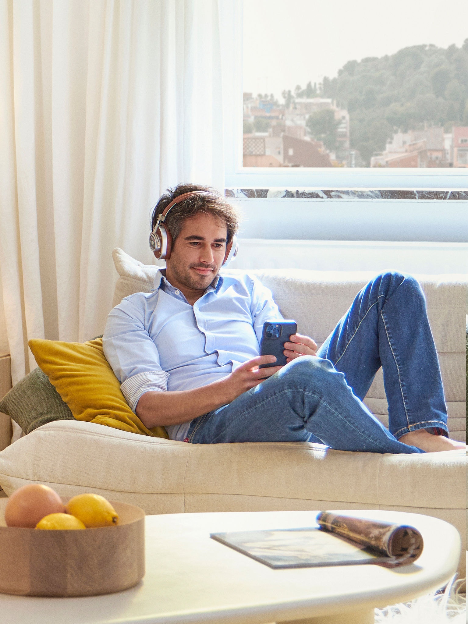 En mand med hovedtelefoner på slapper af på sin sofa, mens han kigger på sin smartphone.