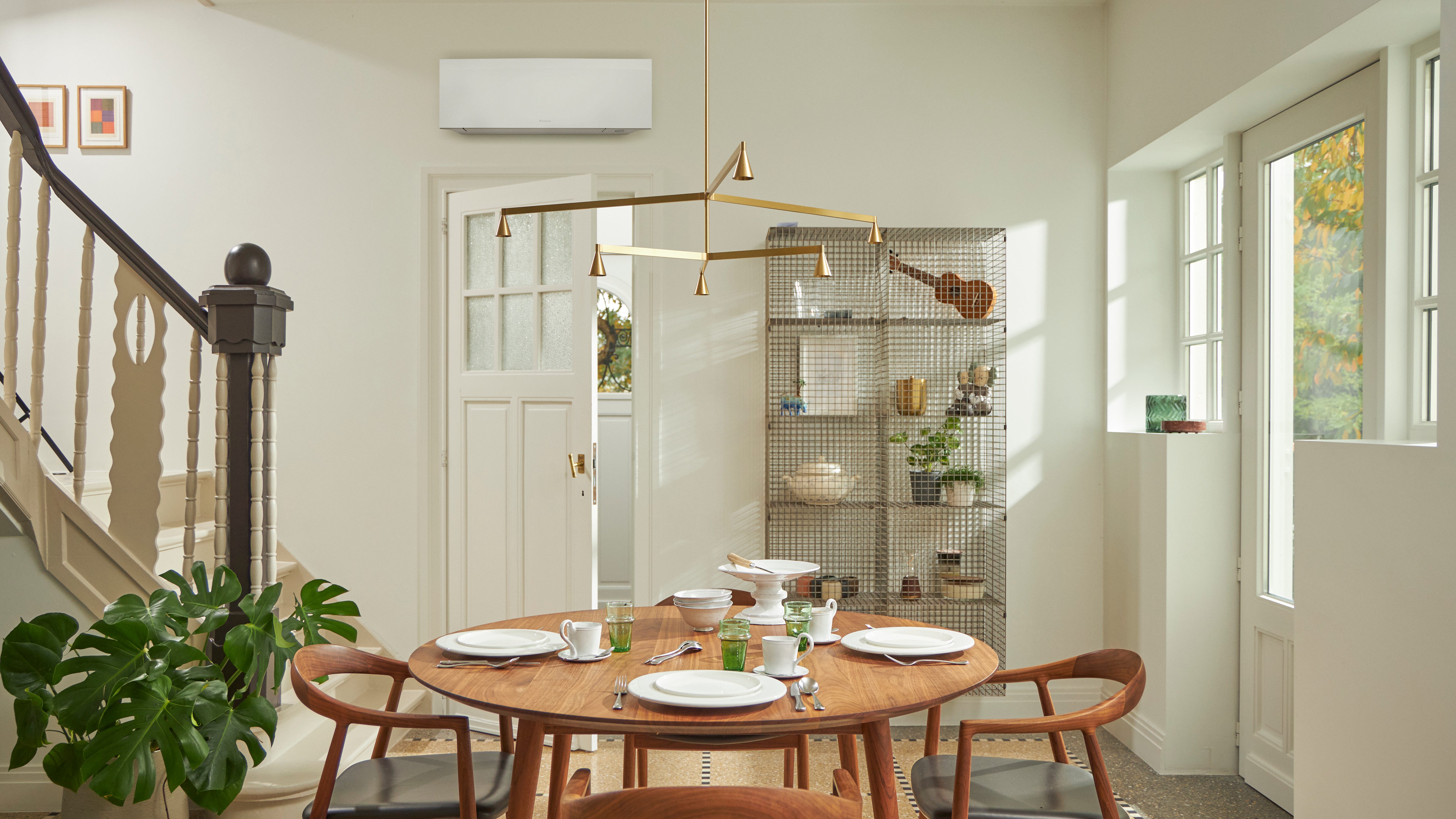 Værelse med et stort vindue, et træbord og en sort, vægmonteret klimaløsning.