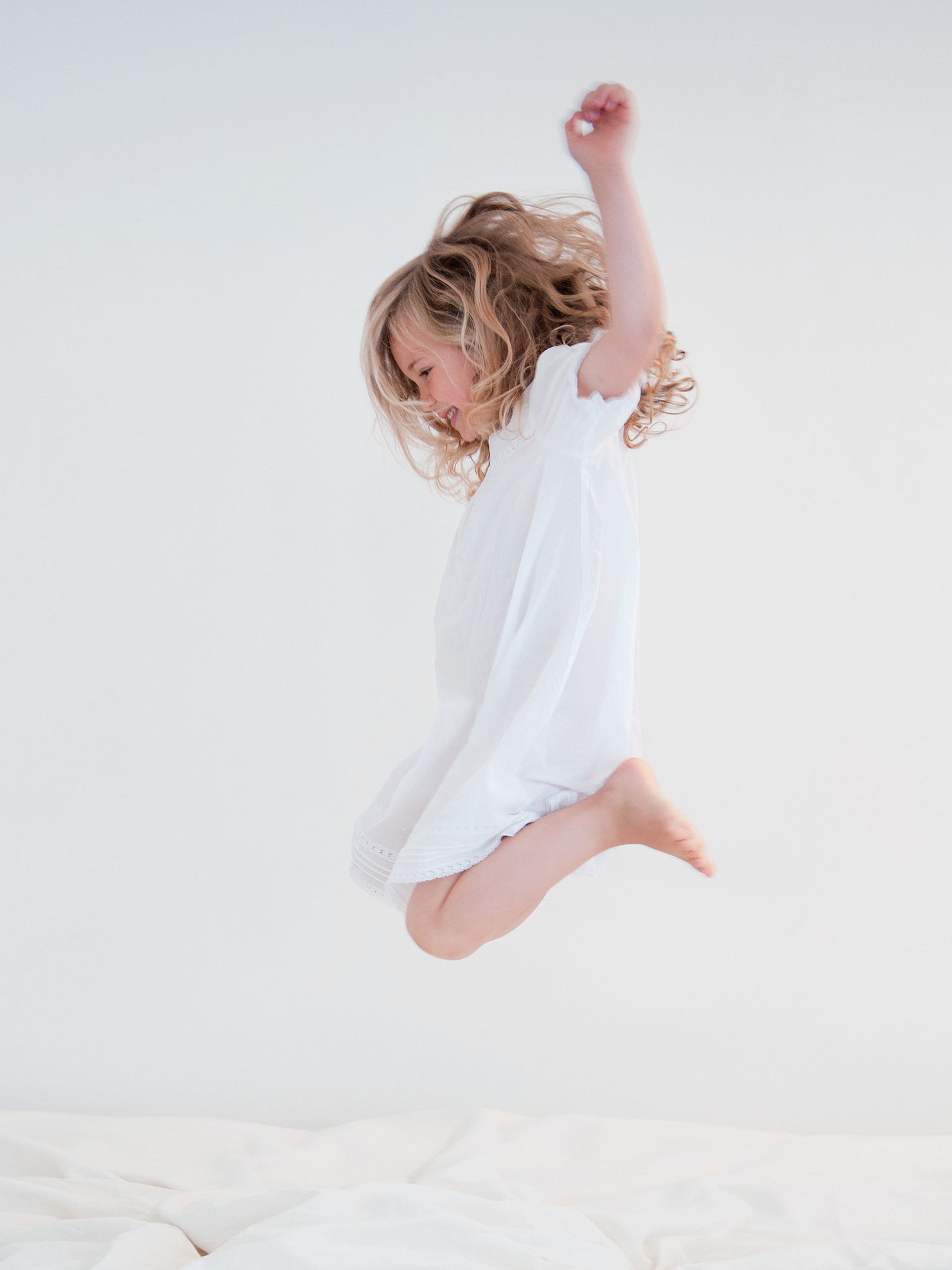 Lille pige i hvid kjole, der hopper på en hvid seng.
