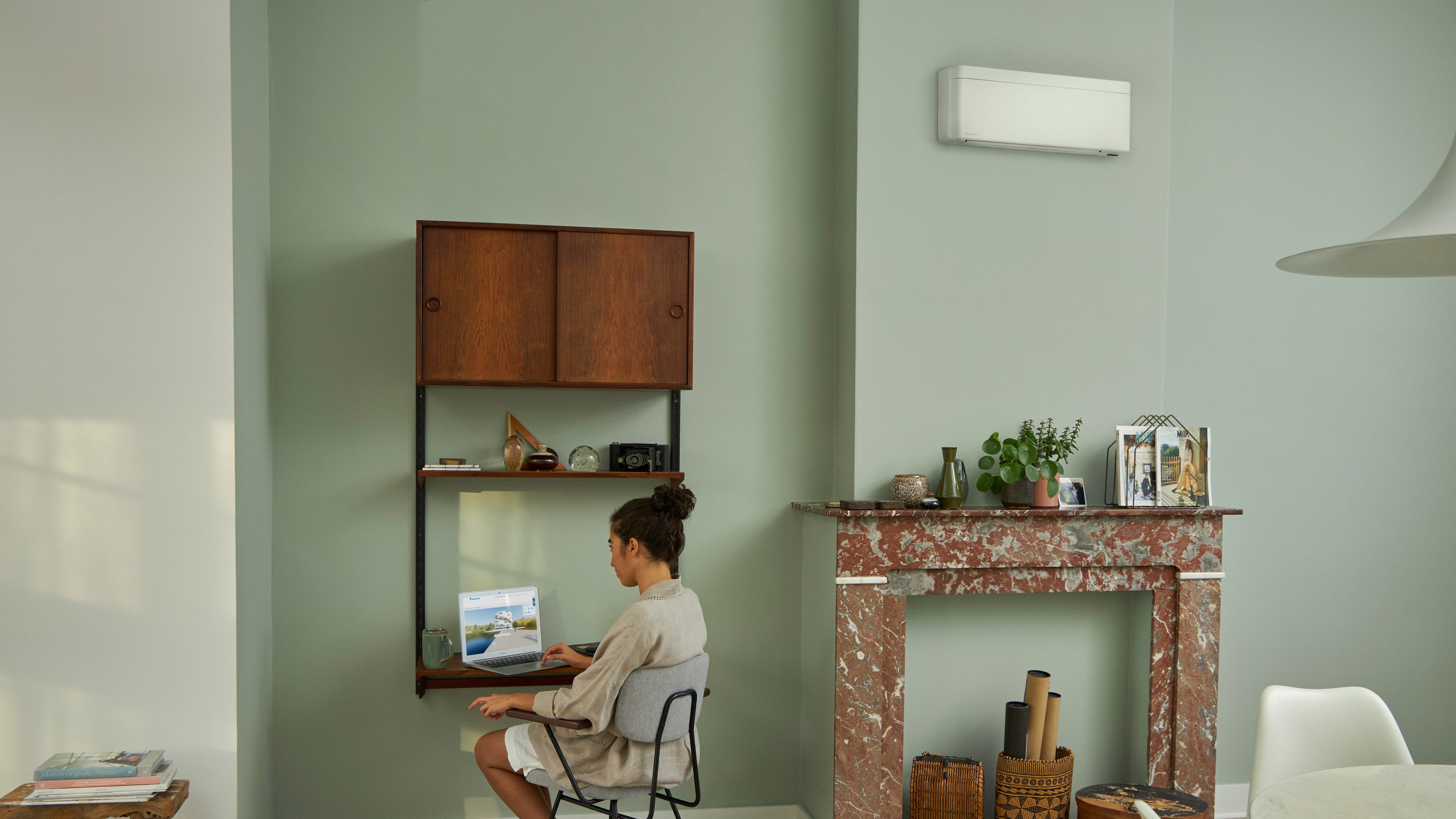 En kvinde besøger Daikins virtuelle oplevelsescenter på sin bærbare computer ved et lille skrivebord i en smukt indrettet stue.